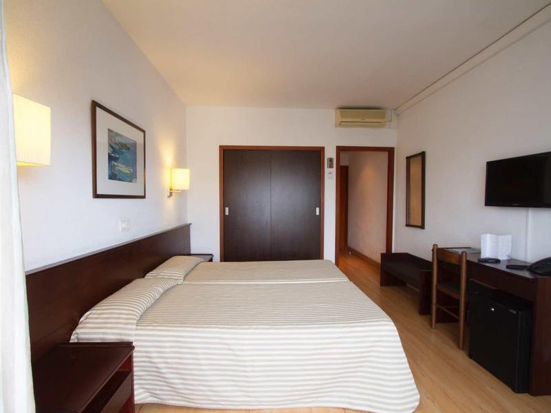 Camera d'hotel pulita con letto matrimoniale, mobili in legno, TV a parete e illuminazione luminosa.