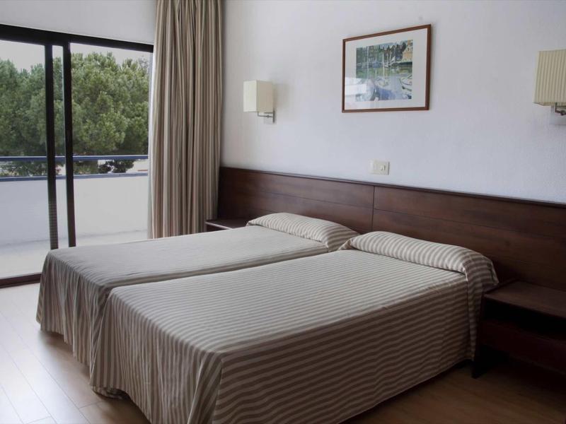 Camera d'hotel con due letti singoli, testiera in legno e porta finestra scorrevole per balcone.