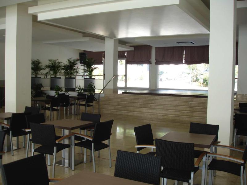 Area pranzo moderna dell'hotel con sedie nere, tavoli in legno e grandi finestroni con tende.