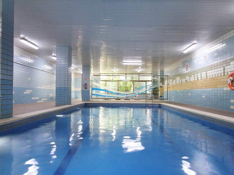 Piscina interna con piastrelle blu e grandi finestre che lasciano entrare la luce naturale.