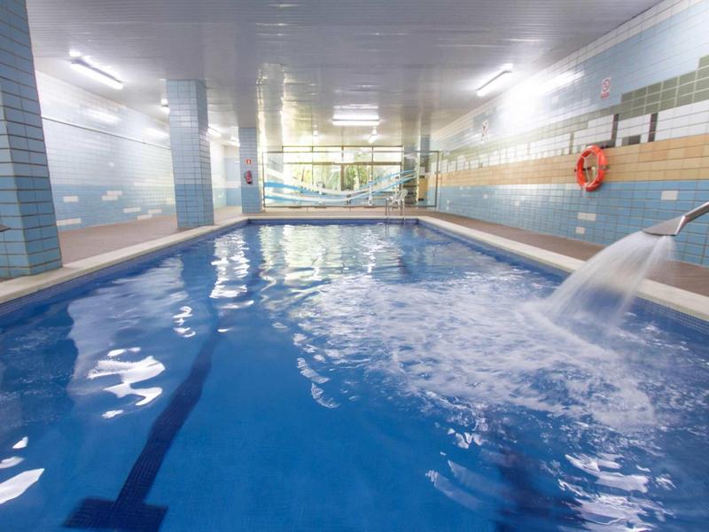 Piscina interna con acqua corrente e pareti piastrellate, atmosfera luminosa e spaziosa.