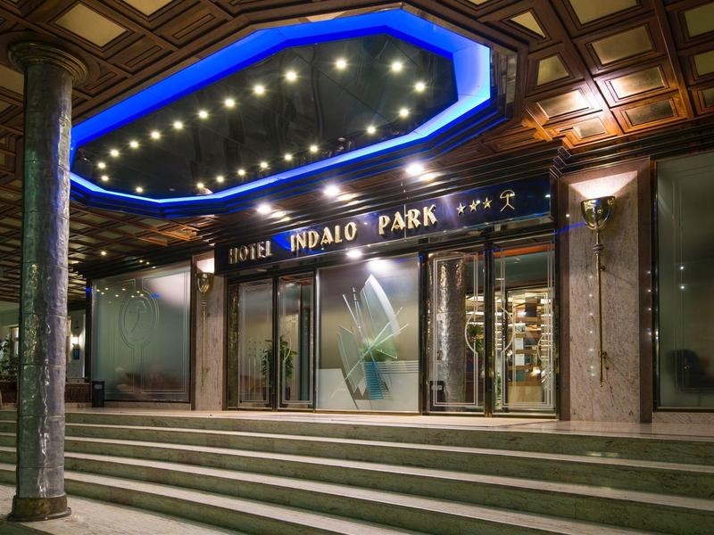 Beleuchteter Hoteleingang mit Treppen und verzierten Holzdecke bei Nacht.