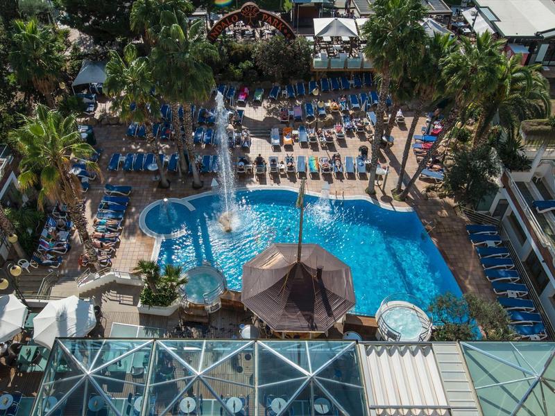 Blick auf einen großen Hotelpool mit blauen Liegestühlen und Palmen.