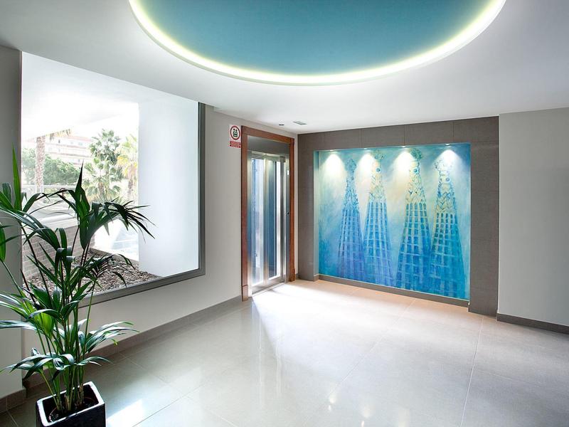 Heller moderner Raum mit großen Fenstern, Pflanzen und blau beleuchtetem Wasserfall an der Wand.