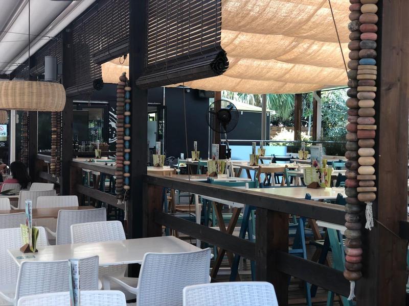 Hell dekorierter Außenbereich eines Restaurants mit weißen Stühlen und Tischen unter Sonnensegeln.