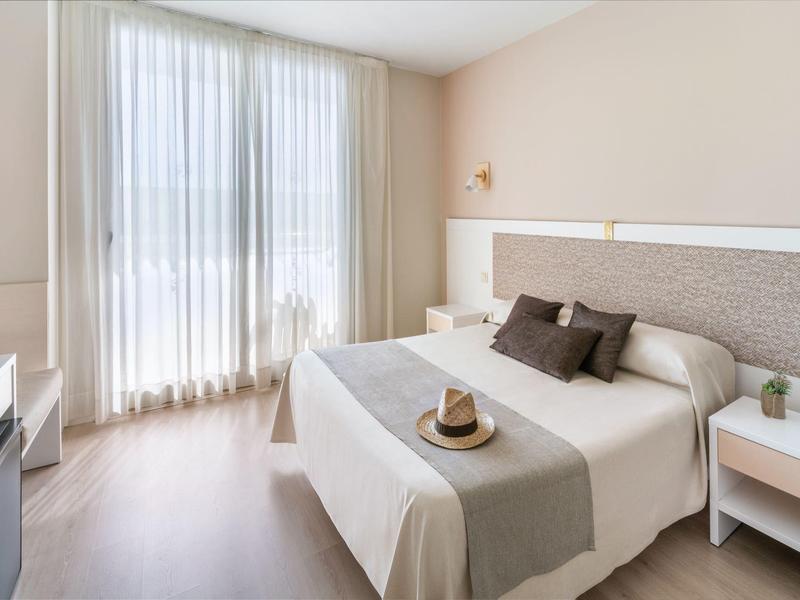 Helles Hotelzimmer mit Doppelbett, beigen Vorhängen und minimalistischer Einrichtung.