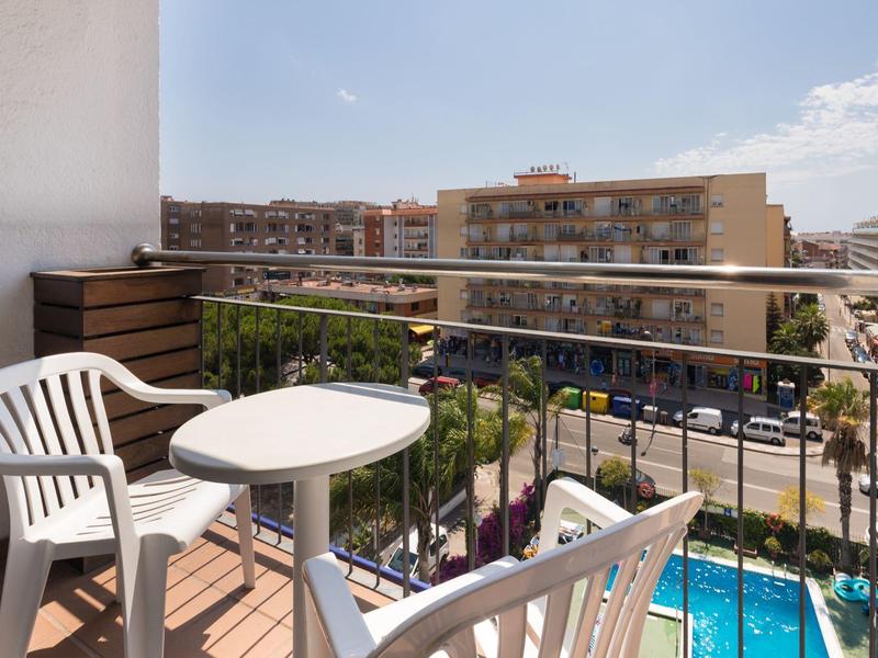Balcony with white chairs and table overlooking a pool and apartment buildings.