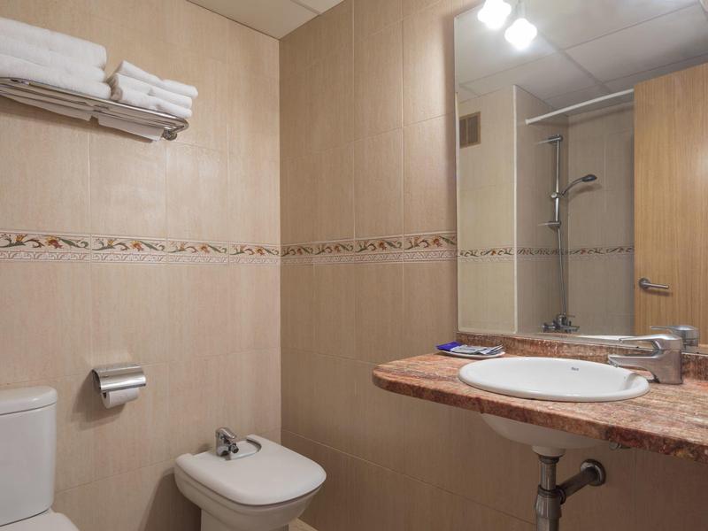 Neat hotel bathroom with toilet, bidet, sink, mirror, and stacked towels on towel rack.