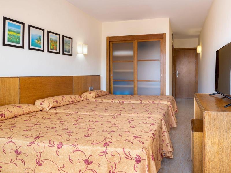 Hotel room with two beds, floral bedspreads, framed art, and wood furniture including TV stand.