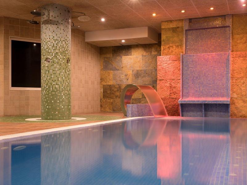 Indoor pool with waterfall and soft lighting in a luxurious spa area.