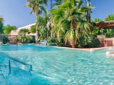 Grande piscina all'aperto con acqua limpida, circondata da palme e lettini in un resort.