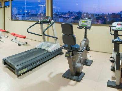 Palestra moderna con tapis roulant, cyclette e attrezzi per forza con vista sulla città al crepuscolo.