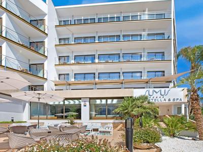 Vícepodlažní hotelová budova s balkony, venkovní terasou a palmami pod modrou oblohou.