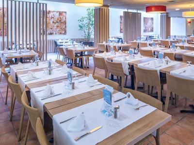 Světlá restaurace s dřevěnými stoly a židlemi, prostřená s bílými ubrousky a jídelními lístky.