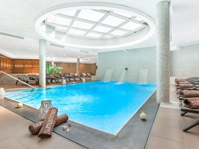 Vnitřní bazén s modrým osvětlením, lehátky a moderním designem v uvolněné atmosféře.