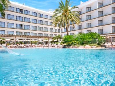 Hotel s velkým bazénem, palmami a lehátky pod modrou oblohou