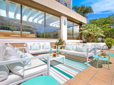 Světlá terasa s bílým posezením, barevným kobercem a výhledem na zahradu a palmy.