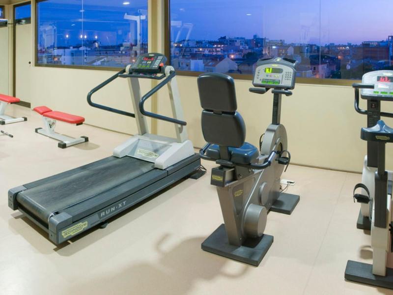 Světelná posilovna s tréninkovým vybavením a velkými okny s výhledem na město.