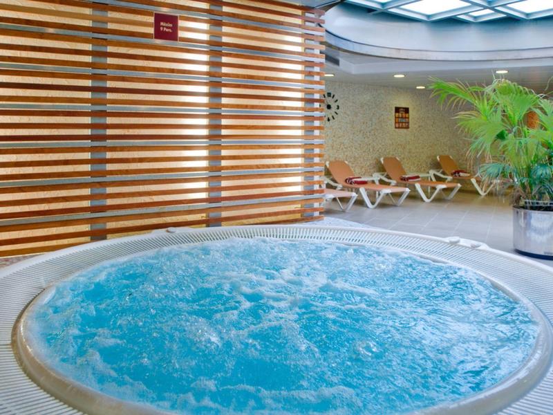 Kruhový vířivý bazén s bublající vodou v moderní wellness zóně s lehátky.