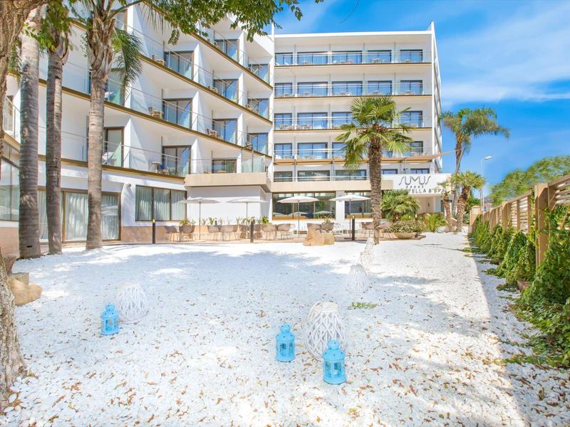 Moderní hotelový komplex s písečnou pláží, palmami a lehátky pod modrou oblohou.