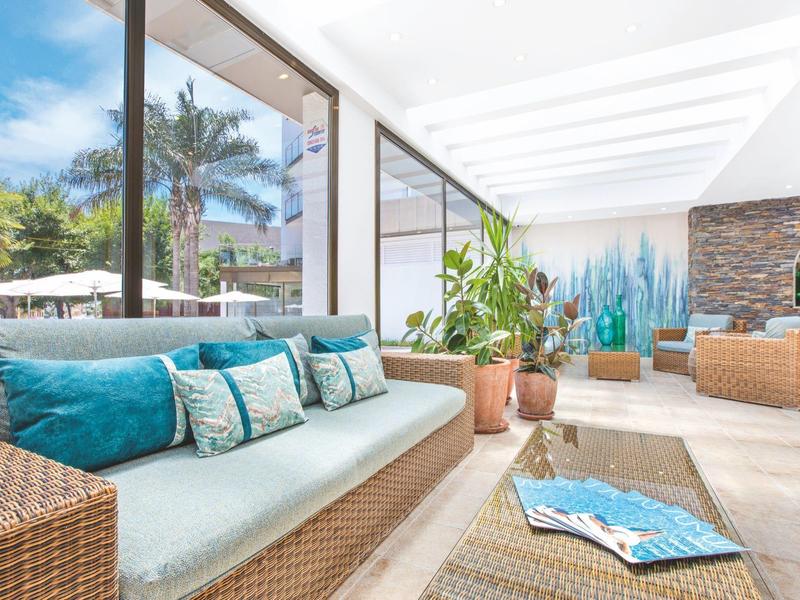 Světlá, moderní lounge s ratanovým nábytkem a modrými polštáři v hotelu.