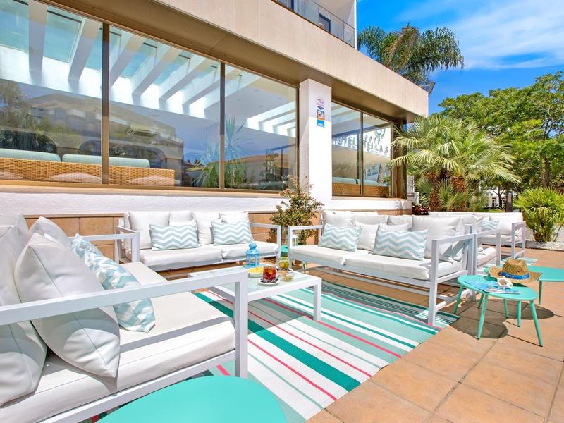 Světlá terasa s bílým posezením, barevným kobercem a výhledem na zahradu a palmy.
