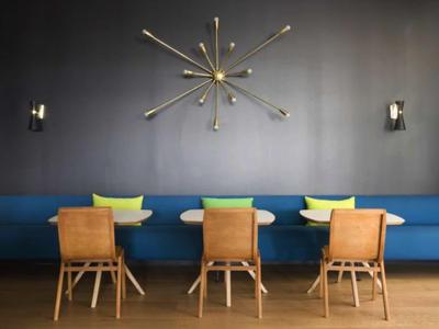 Moderner Essbereich mit blauer Bank, Holztischen, Stühlen und kunstvoller Wanduhr in Gold.