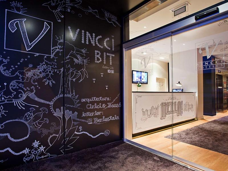 Moderner Büroeingang mit Glaswand, leuchtendem Schriftzug und künstlerischen Wandzeichnungen.