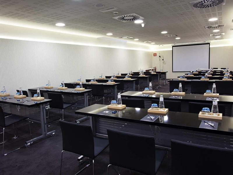 Moderner Seminarraum mit schwarzen Tischen und Stühlen, Projektor und Beamer-Leinwand.