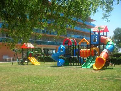 Area giochi colorata con scivoli e strutture per arrampicata su un prato di fronte a un hotel.