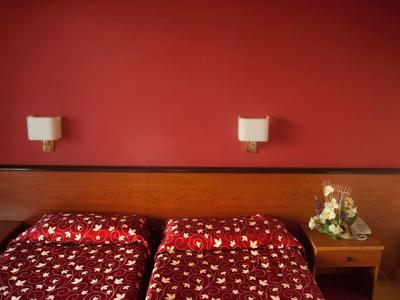 Due letti singoli con coperte rosse davanti a una parete rossa e comodino con composizione floreale.