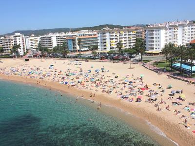Ampia spiaggia di sabbia con molti bagnanti davanti a hotel moderni e acqua di mare limpida.