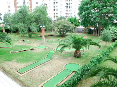 Campo da mini golf con prato artificiale verde, circondato da alberi e palazzi residenziali.