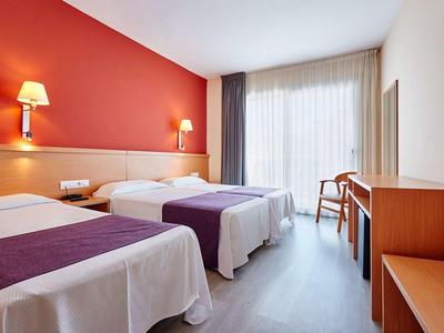 Camera d'hotel con due letti singoli, parete rossa, scrivania e finestra con tende.