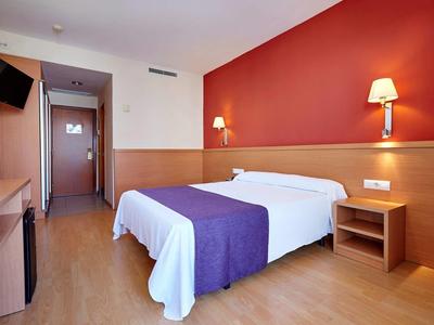 Camera d'hotel moderna con letto matrimoniale, parete rossa e TV a parete.