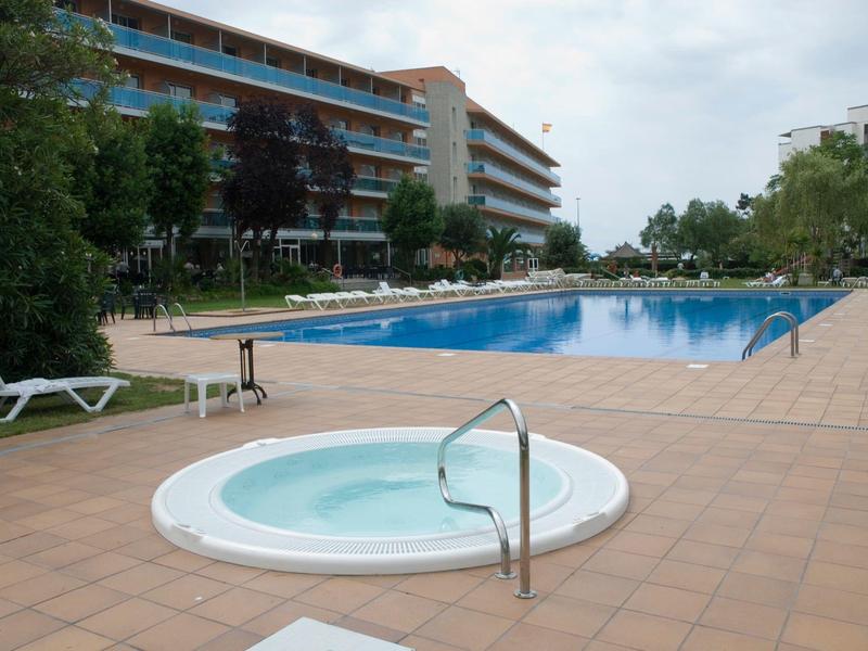 Area esterna dell'hotel con vasca idromassaggio, grande piscina e lettini su pavimento piastrellato.