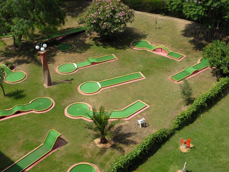 Campo da mini golf con diverse piste e aree verdi, circondato da alberi e cespugli.