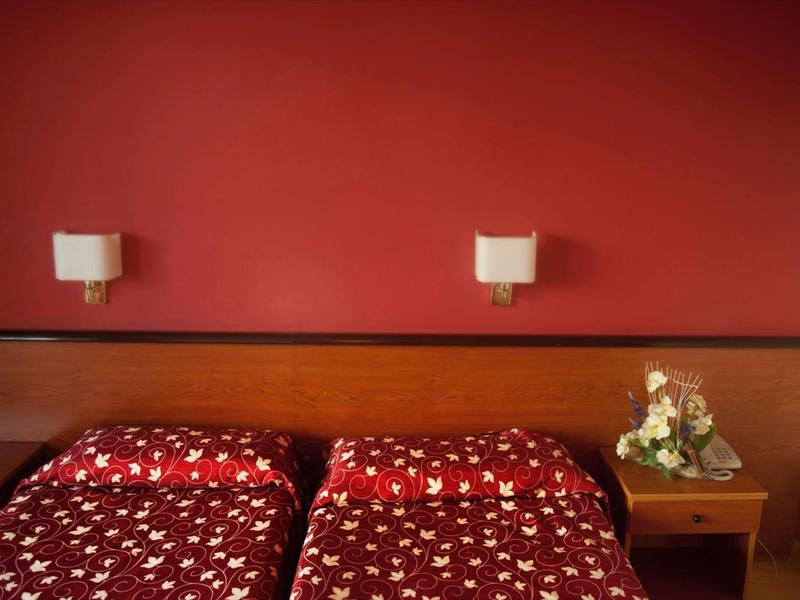 Due letti singoli con coperte rosse davanti a una parete rossa e comodino con composizione floreale.