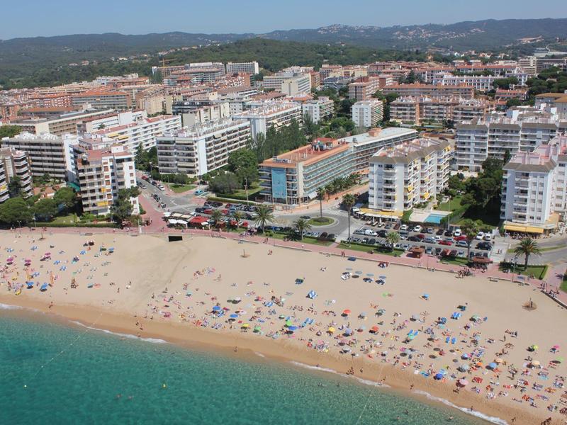 Vista di una spiaggia sabbiosa affollata con molti bagnanti e una città sullo sfondo.