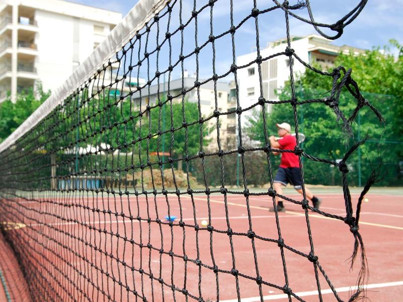 Vista attraverso una rete da tennis strappata su un giocatore in un campo esterno.