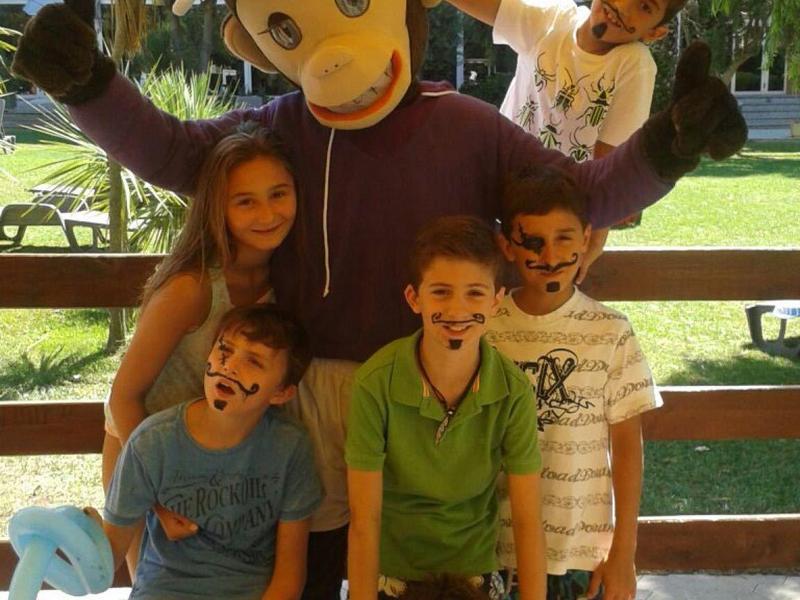 Bambini con una persona in un grande costume da scimmia in un'area giardino soleggiata.