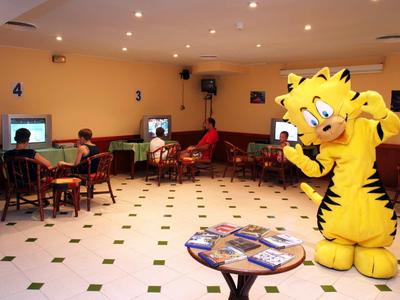Innenraum mit Computern, mehreren Sitzplätzen, gelbem Tigermaskottchen und Tisch mit Zeitschriften.