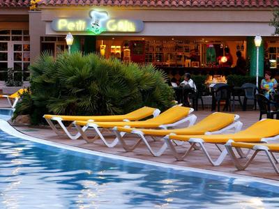 Schwimmbad mit gelben Liegestühlen und grünen Pflanzen vor einer Bar mit Neonlicht.