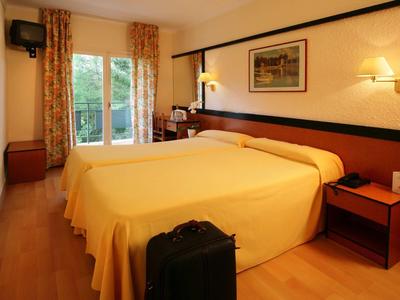 Gemütliches Hotelzimmer mit Doppelbett, Holzmöbeln, Gardinen und einem Koffer am Fußende.