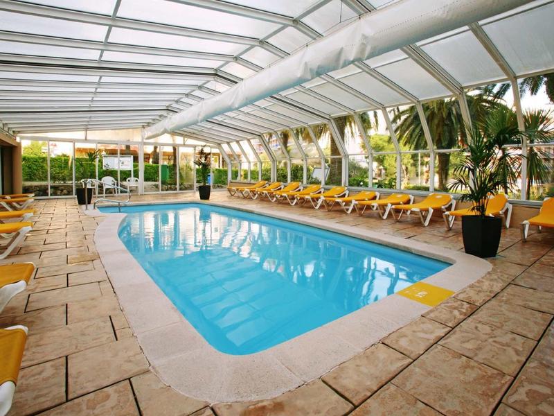 Vnitřní vyhřívaný bazén se žlutými lehátky a skleněnou střechou v hotelu.