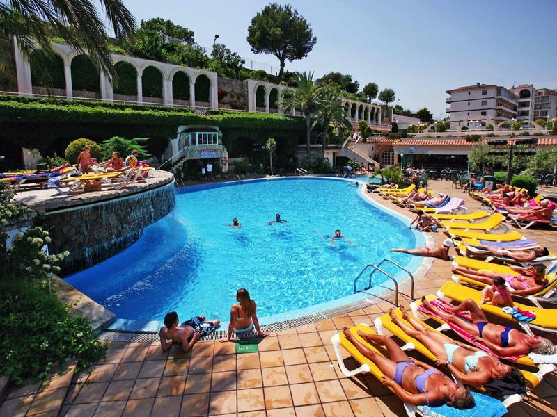 Rušná oblast u bazénu s lehátky a hosty ve slunném rekreačním středisku.