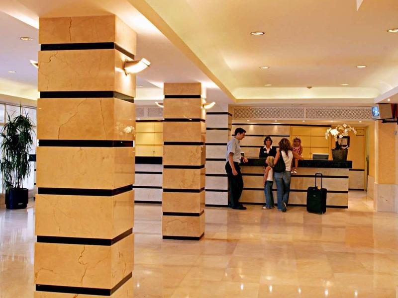 Světlá hotelová lobby s dekorativními sloupy, recepcí a moderním nástěnným uměním.