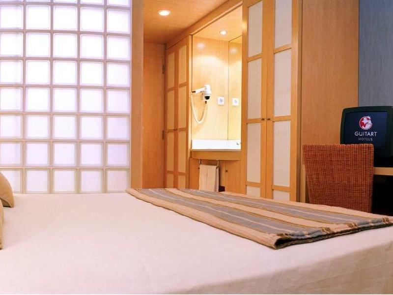 Moderně zařízený hotelový pokoj s velkou postelí, polštáři a psacím stolem.