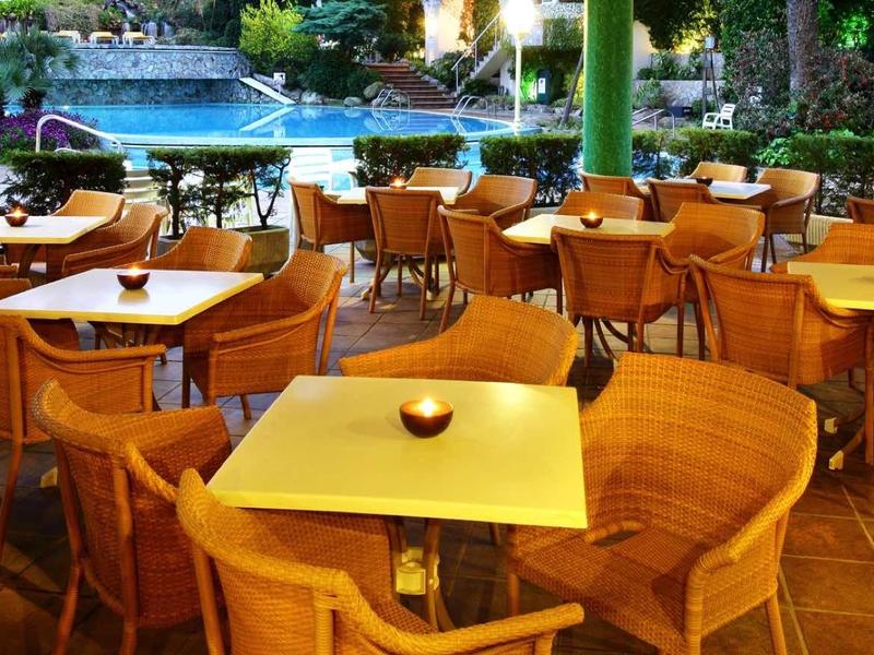 Pohodlná venkovní plocha s dřevěnými stoly a židlemi vedle hotelového bazénu.