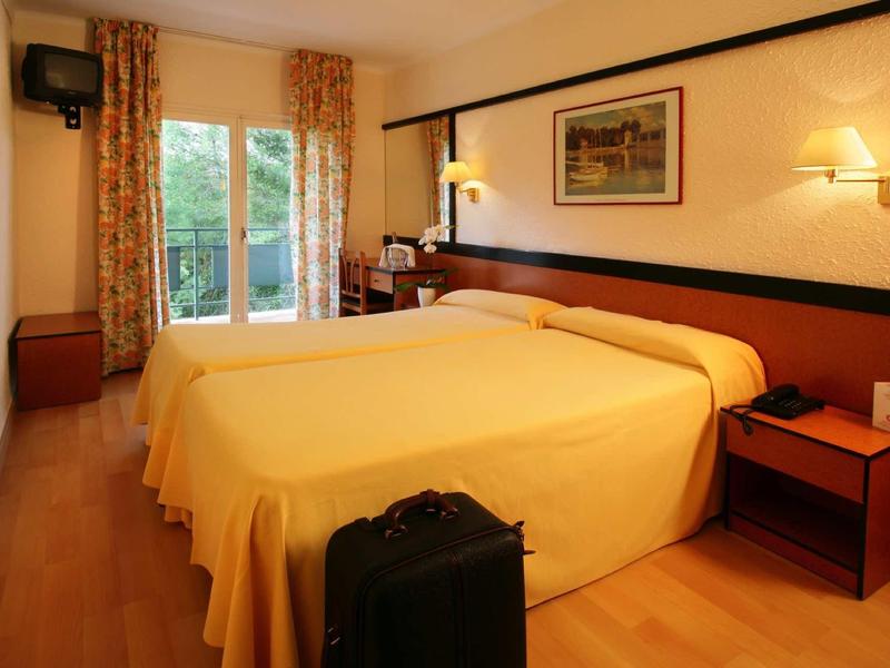 Pohodlný hotelový pokoj se dvěma samostatnými postelemi, nočním stolkem a kufrem u nohou postelí.